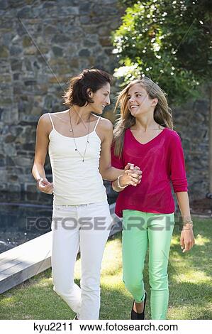 Stock Image - Smiling mother and daughter walking and holding each other's hands. Fotosearch