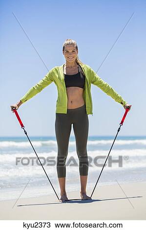 Smiling woman exercising with a chest expander on the beach View Large Photo Image Stock Image - Smiling woman exercising with a chest expander on the beach. Fotosearch