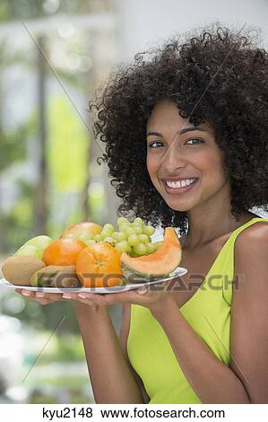Stock Photo - Smiling woman holding a plate of fruits. Fotosearch