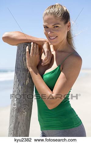 Smiling woman leaning against a wooden post on the beach View Large Photo Image Stock Image - Smiling woman leaning against a wooden post on the beach. Fotosearch