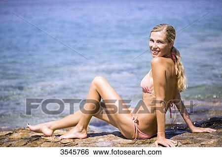 Smiling young woman sitting on the rock at the seaside View Large Photo Image Stock Photograph - Smiling young woman sitting on the rock at the seaside. Fotosearch