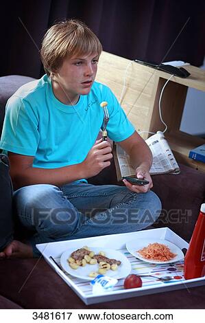 Teenager eating out of a meal tray and watching TV. View Large Photo Image Stock Photo - Teenager eating out of a meal tray and watching TV.. Fotosearch