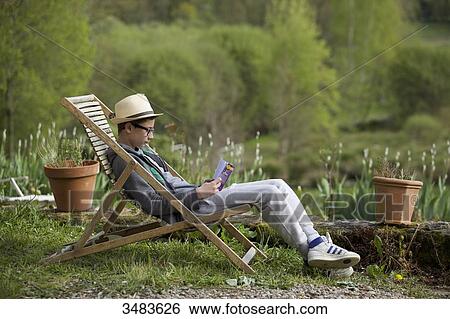 Stock Photograph - Tennager reading a book in a deckchair. Fotosearch