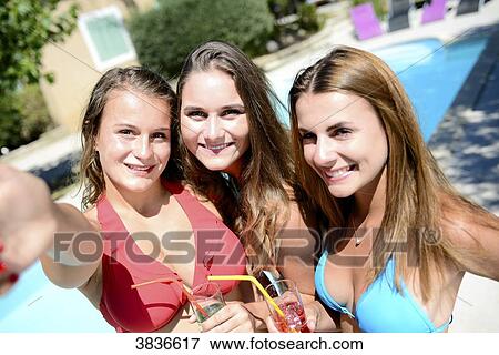 Three beautiful young woman making selfie together by the poolside of resort swimming pool during holiday sunny summer day. View Large Photo Image Stock Photo - Three beautiful young woman making selfie together by the poolside of resort swimming pool during holiday sunny summer day.. Fotosearch