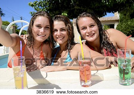 Three beautiful young woman making selfie together by the poolside of resort swimming pool during holiday sunny summer day. View Large Photo Image Stock Photo - Three beautiful young woman making selfie together by the poolside of resort swimming pool during holiday sunny summer day.. Fotosearch