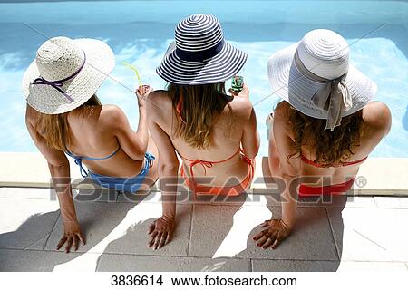 Three beautiful young woman with swimsuit and sun hat sitting by the poolside of resort swimming pool during summer holiday. View Large Photo Image Picture - Three beautiful young woman with swimsuit and sun hat sitting by the poolside of resort swimming pool during summer holiday.. Fotosearch