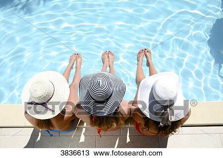 Three beautiful young woman with swimsuit and sun hat sitting by the poolside of resort swimming pool during summer holiday. View Large Photo Image Stock Image - Three beautiful young woman with swimsuit and sun hat sitting by the poolside of resort swimming pool during summer holiday.. Fotosearch