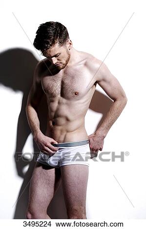 Topless man, against a white wall; wearing white pants, serious, hard shadow on the wall, looking down inside his pants. View Large Photo Image Picture - Topless man, against a white wall; wearing white pants, serious, hard shadow on the wall, looking down inside his pants.. Fotosearch