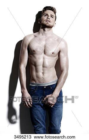 Stock Image - Topless man against a white wall; wearing jeans, serious, mouth slightly open, looking up, hard shadow on the wall. Fotosearch