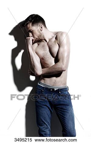 Topless man against a white wall; wearing jeans, serious, hard shadow on the wall, looking down, hand covering his mouth, top botton undone, face in profile View Large Photo Image Stock Photography - Topless man against a white wall; wearing jeans, serious, hard shadow on the wall, looking down, hand covering his mouth, top botton undone, face in profile. Fotosearch