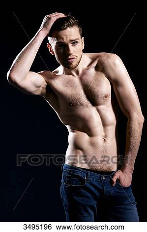 Stock Photograph - Topless man, black background; one hand in his hair, arm up, wearing jeans, serious.. Fotosearch