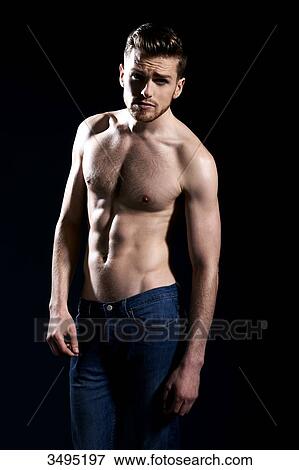 Stock Photo - Topless man, black background; wearing jeans, serious, frowning, on arm alongside his body. Fotosearch
