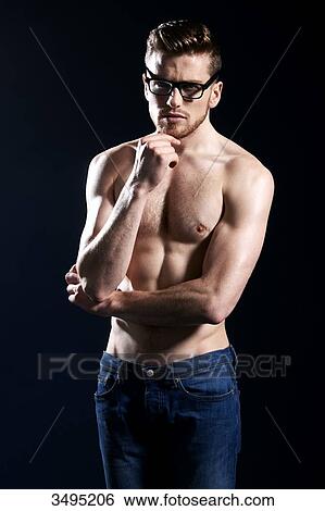 Stock Photograph - Topless man, dark blue background; wearing jeans, serious, one hand on his chin, wearing glasses. Fotosearch