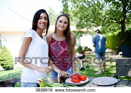 Two beautiful young woman in the garden preparing tomato salad for barbecue party during summer holiday. View Large Photo Image Stock Photograph - Two beautiful young woman in the garden preparing tomato salad for barbecue party during summer holiday.. Fotosearch