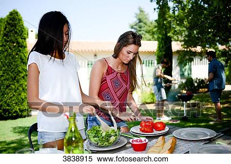 Two beautiful young woman in the garden preparing tomato salad for barbecue party during summer holiday. View Large Photo Image Stock Photography - Two beautiful young woman in the garden preparing tomato salad for barbecue party during summer holiday.. Fotosearch