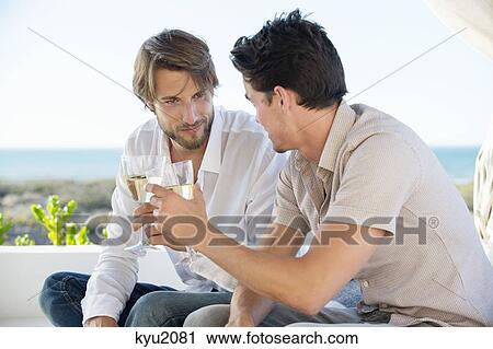 Stock Image - Two male friends toasting with wine. Fotosearch