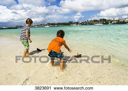 Two young boys, 5 and 7 years old, playing with small boat in coco ont he beach, Gosier island, Guadeloupe, France View Large Photo Image Stock Image - Two young boys, 5 and 7 years old, playing with small boat in coco ont he beach, Gosier island, Guadeloupe, France. Fotosearch