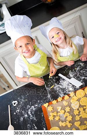 Two young kids happy childrens boy and girl family with apron and chef hat preparing funny cookies in kitchen at home. View Large Photo Image Stock Image - Two young kids happy childrens boy and girl family with apron and chef hat preparing funny cookies in kitchen at home.. Fotosearch