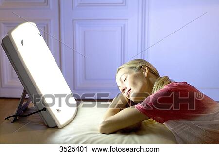 Stock Image - Woman doing a session of light therapy. Fotosearch