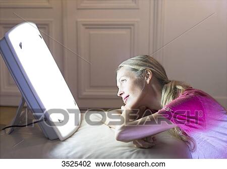 Stock Image - Woman doing a session of light therapy. Fotosearch