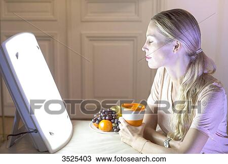 Stock Image - Woman doing a session of light therapy. Fotosearch