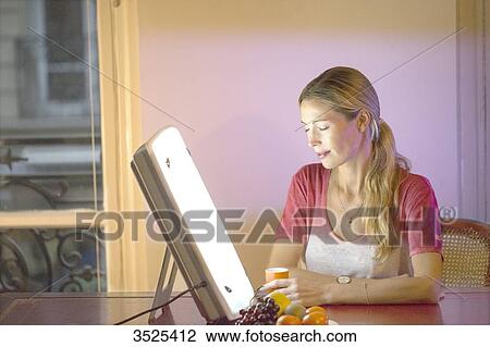 Stock Image - Woman doing a session of light therapy. Fotosearch