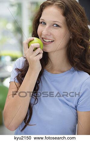 Stock Image - Woman eating a green apple and smiling. Fotosearch