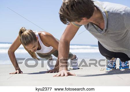 Stock Photo - Woman exercising on the beach with her coach. Fotosearch