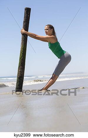 Stock Photo - Woman exercising with a wooden post on the beach. Fotosearch