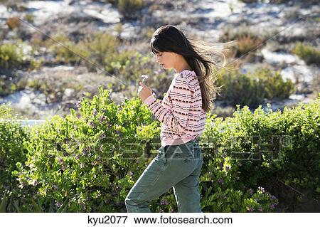 Stock Photo - Woman holding a flower in vegetation. Fotosearch