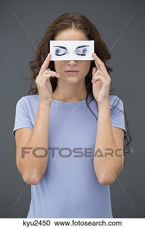 Stock Image - Woman holding a paper with false eyes in front of her face. Fotosearch