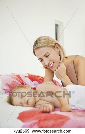 Woman looking at her baby sleeping on the bed View Large Photo Image Stock Photo - Woman looking at her baby sleeping on the bed. Fotosearch