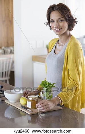 Stock Image - Woman preparing herbal tea in the kitchen. Fotosearch
