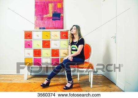Picture - Woman sitting on a red chair in a colorful room. Fotosearch