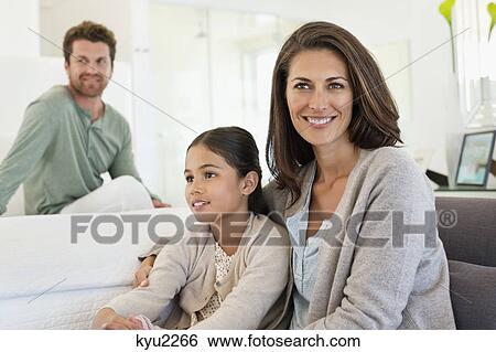 Woman sitting with her daughter and her husband in the background View Large Photo Image Stock Photograph - Woman sitting with her daughter and her husband in the background. Fotosearch