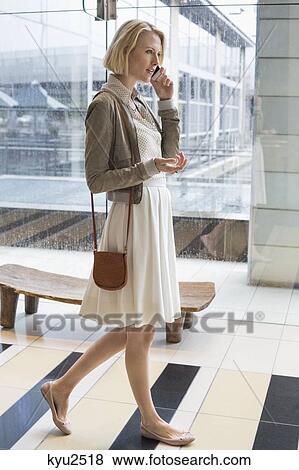 Stock Photo - Woman talking on a mobile phone while walking on an airport. Fotosearch
