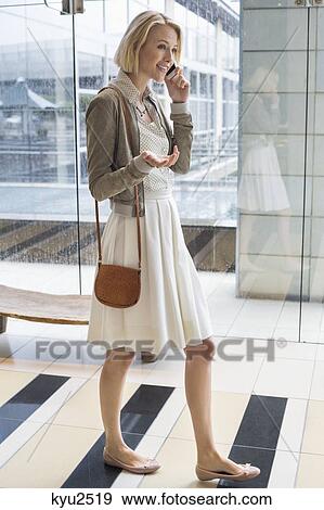 Stock Photo - Woman talking on a mobile phone while walking on an airport. Fotosearch