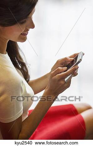 Stock Image - Woman text messaging on a mobile phone and smiling. Fotosearch