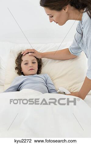 Woman touching forehead of her son looking sick View Large Photo Image Stock Image - Woman touching forehead of her son looking sick. Fotosearch