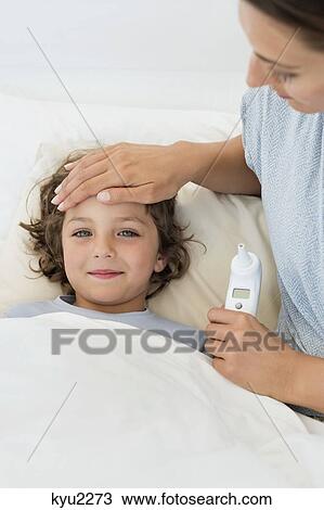Stock Image - Woman touching forehead of her son looking sick. Fotosearch
