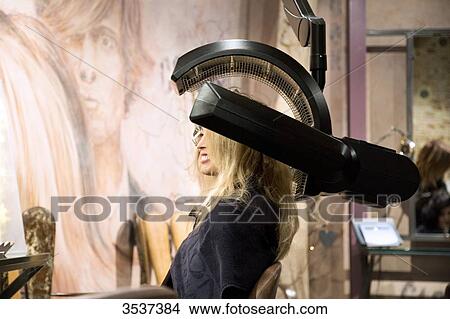 Picture - Woman under a heating apparatus for hair. Fotosearch