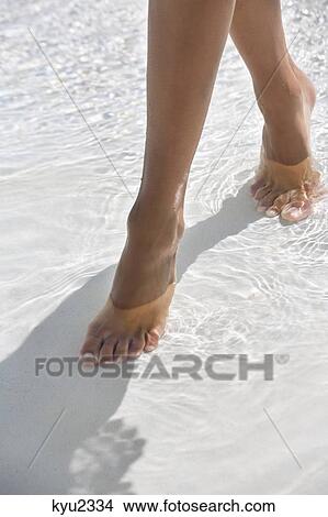 Picture - Woman walking in water on the beach. Fotosearch