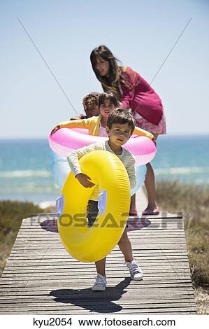 Picture - Woman with her children holding inflatable rings on a boardwalk on the beach. Fotosearch