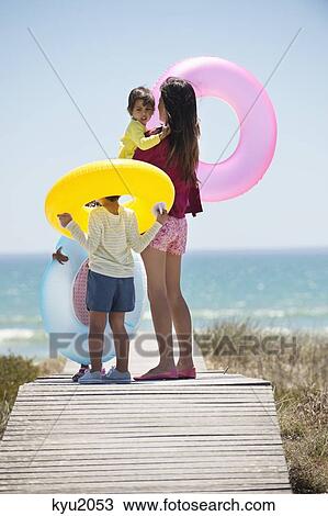 Stock Image - Woman with her children holding inflatable rings on a boardwalk on the beach. Fotosearch
