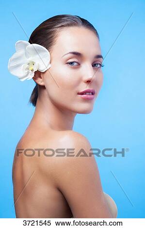 Stock Photography - Young girl with a flower on the ear looking at the objective. Fotosearch