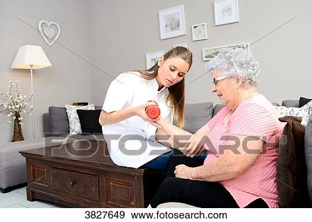 Stock Photo - Young physiotherapist nurse helping elderly women physical rehabilitation at home. Fotosearch