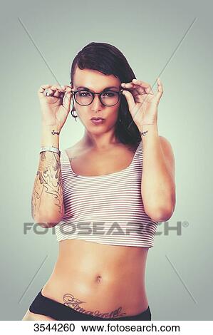 Stock Image - Young tattooed woman holding her glasses. Fotosearch