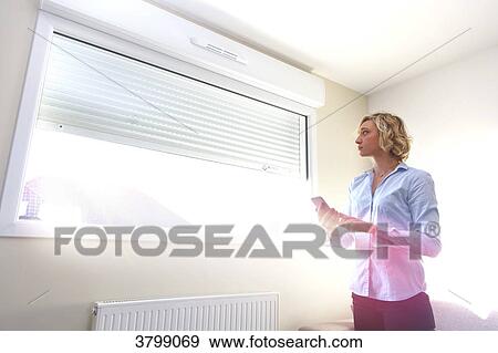 Young woman at home using smartphone to open windows View Large Photo Image Stock Photo - Young woman at home using smartphone to open windows. Fotosearch