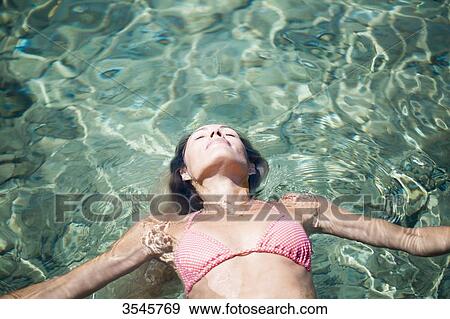 Stock Photo - Young woman floating in the sea. Fotosearch