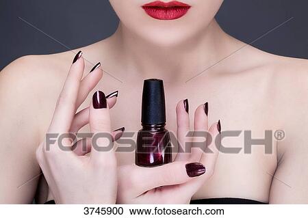 Stock Image - Young woman holding a nail polish bottle. Fotosearch
